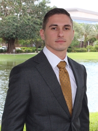 Portrait of a student in a suit and golden brown tie standing outside with a lake in the background