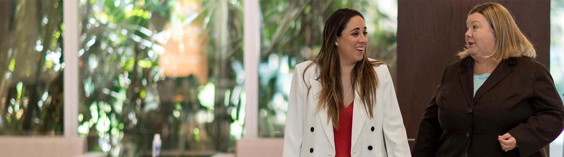 two women in professional attire walking down a hall and talking