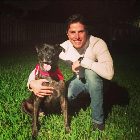 Smiling man hugging a dog outdoors on the grass