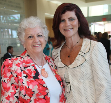 Two professionally-dressed smiling women posing together indoors