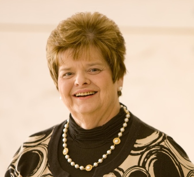 Portrait of a smiling woman wearing a white beaded necklace and black cardigan and shirt on a white background