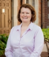 Portrait of a smiling woman in a white dress shirt standing outdoors with plants in the background