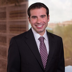 Portrait of a smiling man in a black suit and red and white striped tie standing on a balcony