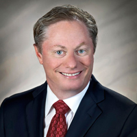 Portrait of a smiling man in a navy suit and red tie on a gray background