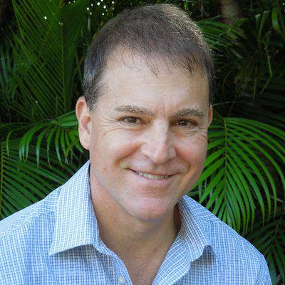 Portrait of a smiling man in a blue and white dress shirt with shrubbery in the background