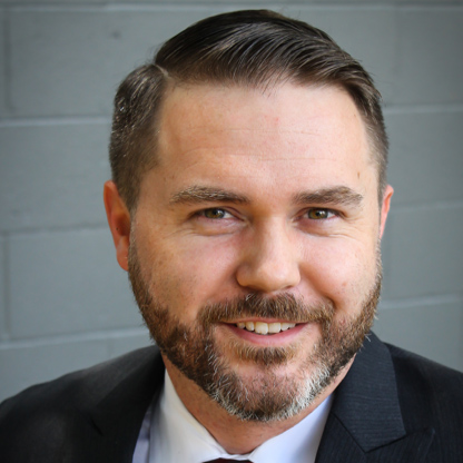 Portrait of a smiling man in a suit with a gray brick wall in the background