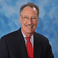 Portrait of a smiling man in a black suit and red tie on a blue background