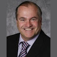 Portrait of a smiling man in a black suit and purple tie on a gray background