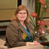 Smiling woman in a brown suit and blue shirt sitting on a brown couch