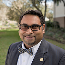 Portrait of a smiling man in a black pinstripe suit standing outdoors