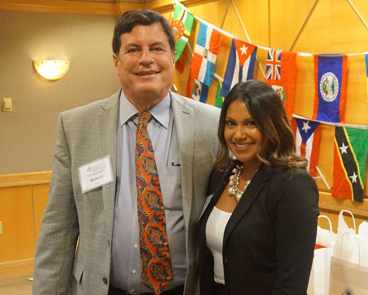 Professionally-dressed man and women standing together and smiling with flags in the background