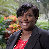 Portrait of a smiling woman wearing black and red with green plants in the background