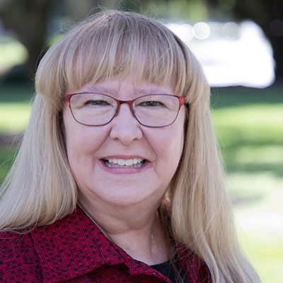 Portrait of a smiling woman wearing black and red with green plants in the background