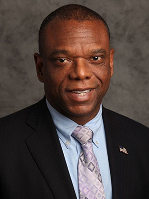 Portrait of a smiling man in a black suit, blue dress shirt and purple tie on a brown background