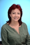 Portrait of a red-haired smiling woman wearing a green shirt on a light blue background
